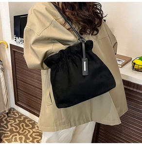 Detail of a black drawstring bucket bag with leather straps and metal tag in lifestyle setting