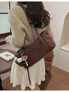 Brown suede shoulder tote bag with unique baseball charms and woven drawstring accents