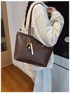 Detail of dark brown woven tote bag featuring beaded charm and Lumoman brand tag