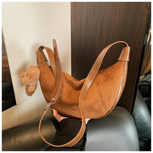 Detail of a brown suede hobo bag with a plush bear charm and adjustable leather strap