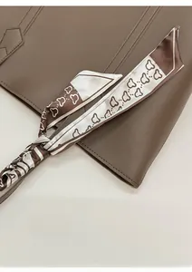 Detail of a brown and white silk twilly scarf with heart patterns tied to a leather bag