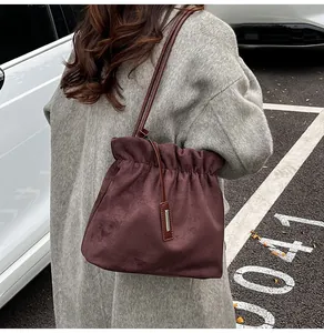 Detail of dark brown suede bucket bag with drawstring closure and silver metal pendant