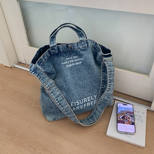 Detail of blue denim tote bag with vintage white lettering and adjustable strap