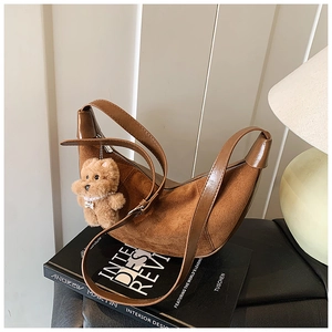 Detailed macro view of a brown crescent shoulder bag with a cute plush bear charm decoration