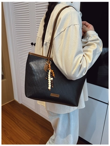Detail of black woven tote bag with brown leather trim and colorful wooden bead tassel