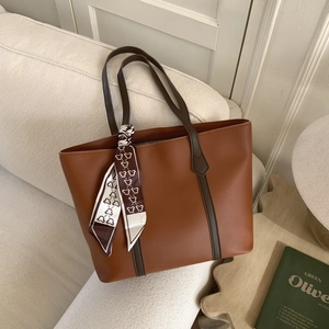 Detailed view of brown leather tote bag with elegant patterned scarf on handle