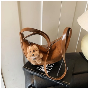 Detailed texture of brown suede crescent bag with plush bear charm and sleek zipper