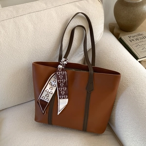 Detail of a brown leather tote bag with a patterned silk scarf on a cozy sofa