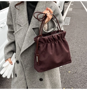 Detail of burgundy suede bucket bag with pleated texture styled with a grey wool coat