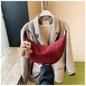 Detail view of burgundy suede crescent bag with a plush bear charm on a suit background