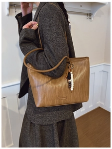 Detail of brown woven tote bag with beaded tassel charm and smooth shoulder straps