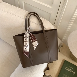 Close-up of a dark brown leather tote bag with a bear print silk scarf on soft sofa
