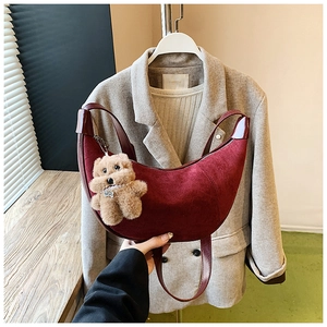 Detailed view of burgundy crescent bag with velvet texture and cute teddy bear charm