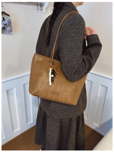 Brown woven texture tote bag with beaded tassel shown worn by a model in a minimalist room