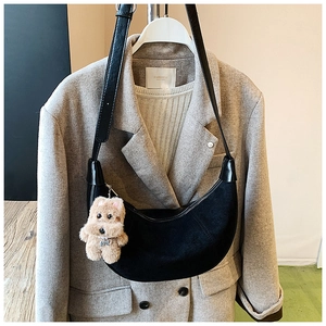 Detail of black suede hobo bag with adjustable strap and cute plush dog charm