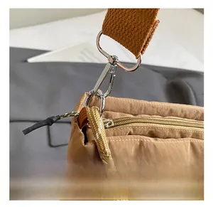 Detail of a bright silver metal hook on a brown nylon bucket bag with woven shoulder strap