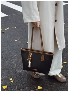 Detail of black woven tote bag with dark brown handles and colorful beaded charm on street