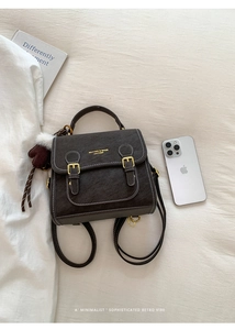 Detail eines dunkelbraunen Lederrucksacks mit Goldschnallen und Plüschbär-Anhänger