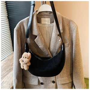 Detail of black crescent hobo bag with teddy bear charm on a khaki wool blazer