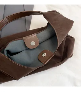 Detail view of the metal magnetic clasp and stitching on the brown leather tote bag