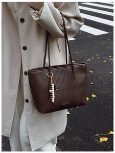 Detail of dark coffee woven tote bag with leather handles and beaded charm in street style