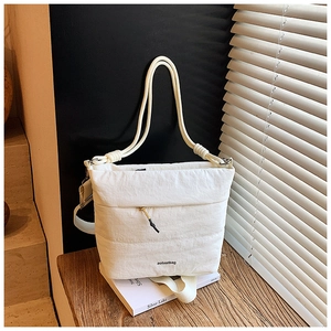 Detail of white quilted tote bag with rope handles on a wooden table with accessories