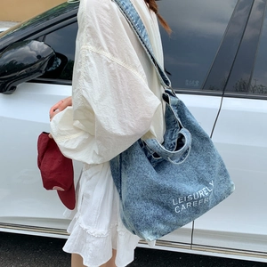 Detail shot of large blue denim bucket bag with LEISURELY CAREFREE print in street style