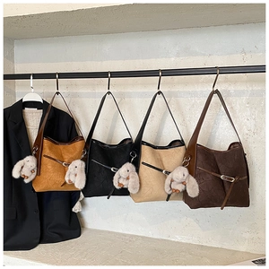 Detail of four pleated tote bags in earth tones with plush bunny charms on hooks