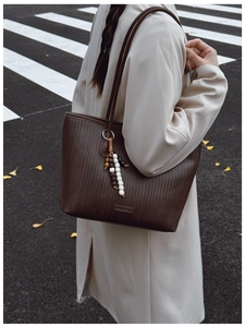 Detail of a brown woven texture tote bag with stylish bead tassel and shoulder strap