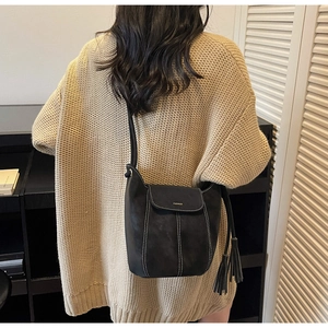 Détail du sac seau noir en cuir mat avec surpiqûres blanches et long ornement à franges