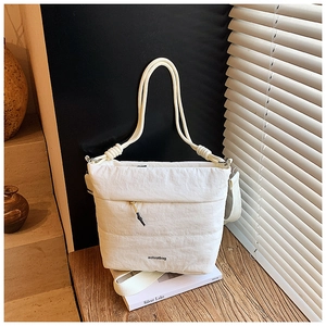 Quilted beige puffy nylon crossbody bag with dual straps on a minimalist wooden table
