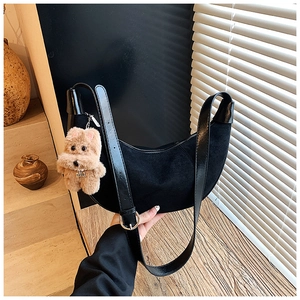Detail of black suede crescent bag with leather strap and cute bear plush charm