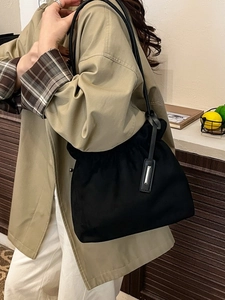 Minimalist black cloud bucket bag with silver buckle worn over shoulder on a trench coat