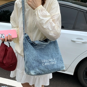 Close-up of light blue denim bucket bag featuring white printed artistic lettering