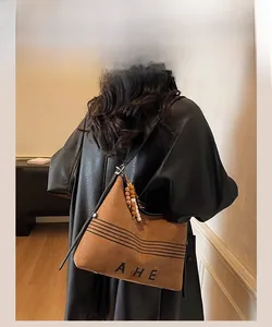 Detail of brown suede bucket bag with AHE lettering and decorative wooden bead pendant