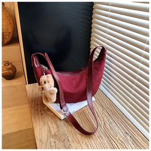 Detail of burgundy crescent shoulder bag with suede texture and cute teddy bear charm