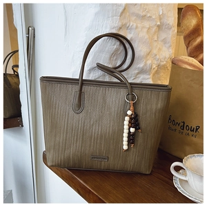 Detail of khaki woven tote bag with wooden bead tassel charm in a lifestyle setting