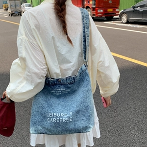 Street style view of a large washed blue denim bucket bag with white printed text decoration