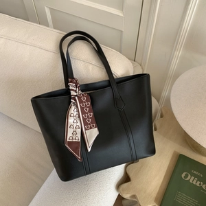 Detail of a black leather tote bag with a decorative floral silk scarf on a sofa