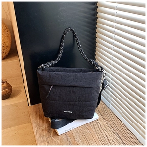 Detail of black nylon bucket bag with knot handle and adjustable strap on a wooden table