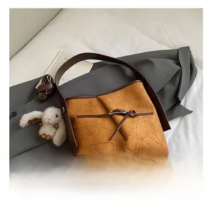Detail of camel bucket bag with wrinkled texture, brown handles and grey rabbit charm