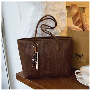 Detail of dark brown woven tote bag featuring a colorful beaded tassel and side logo