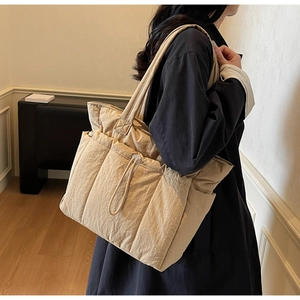Quilted tote bag showing shoulder carry style and side pocket details in beige color