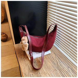 Detail of burgundy suede crescent bag featuring a cute brown plush bear charm and smooth strap