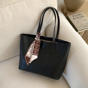 Detail of minimalist black faux leather tote bag featuring a printed small bear scarf charm