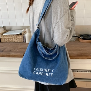 Detail of blue denim bucket bag with white LEISURELY CAREFREE text and adjustable strap