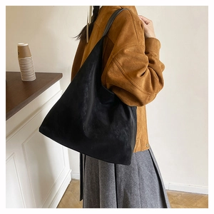 Side view of a large black suede tote bag styled with a brown coat for a chic winter look