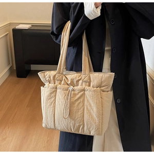 Detail of beige quilted tote bag featuring a front drawstring pocket and nylon texture