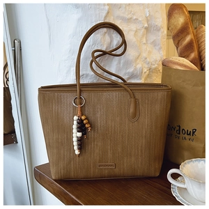 Detail of woven brown leather tote bag with decorative bead tassel in a cozy cafe setting