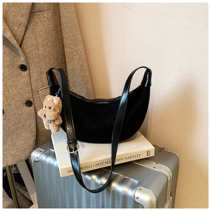 Detail of black crescent hobo bag with plush bear charm on a travel suitcase
